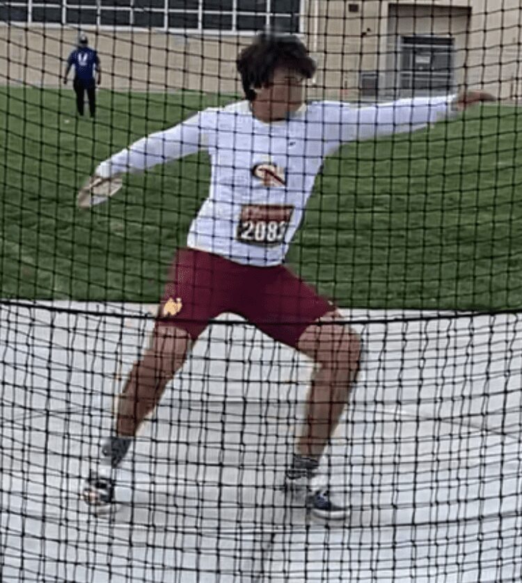 Discus thrower mid-throw inside netted cage