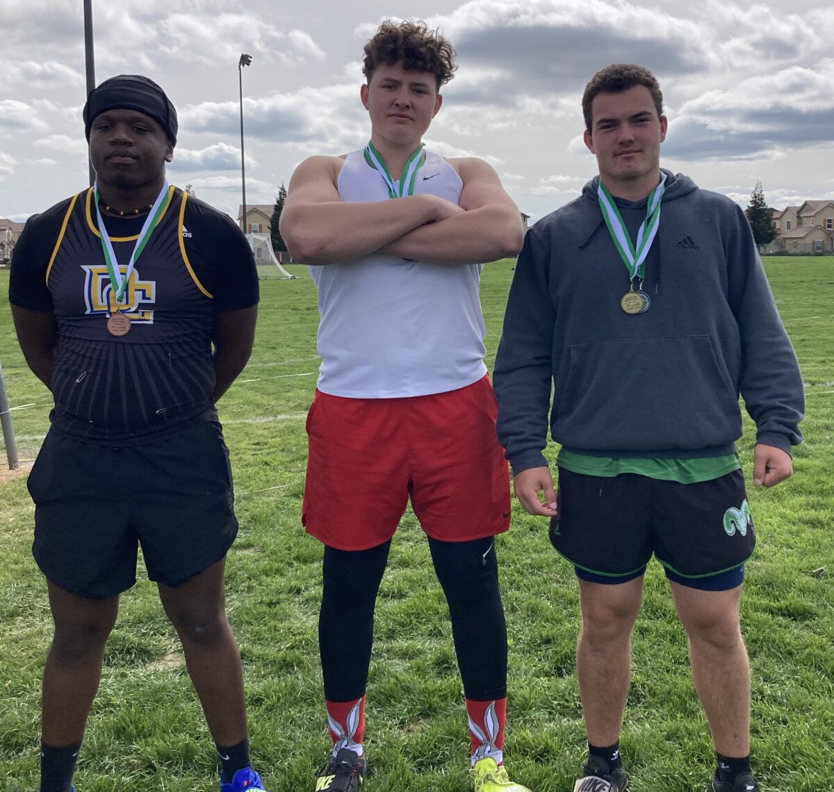 Three athletes wearing medals on grass field