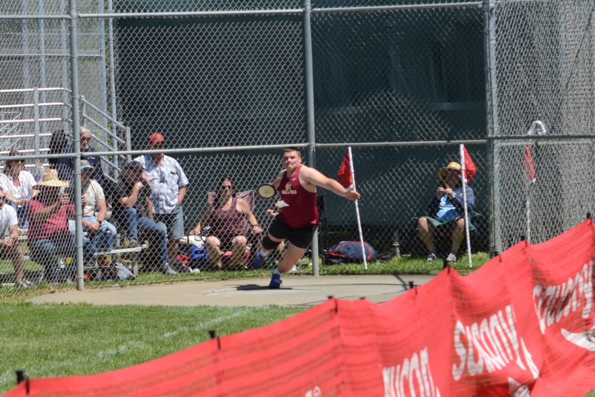 Athlete throwing discus in fenced track meet