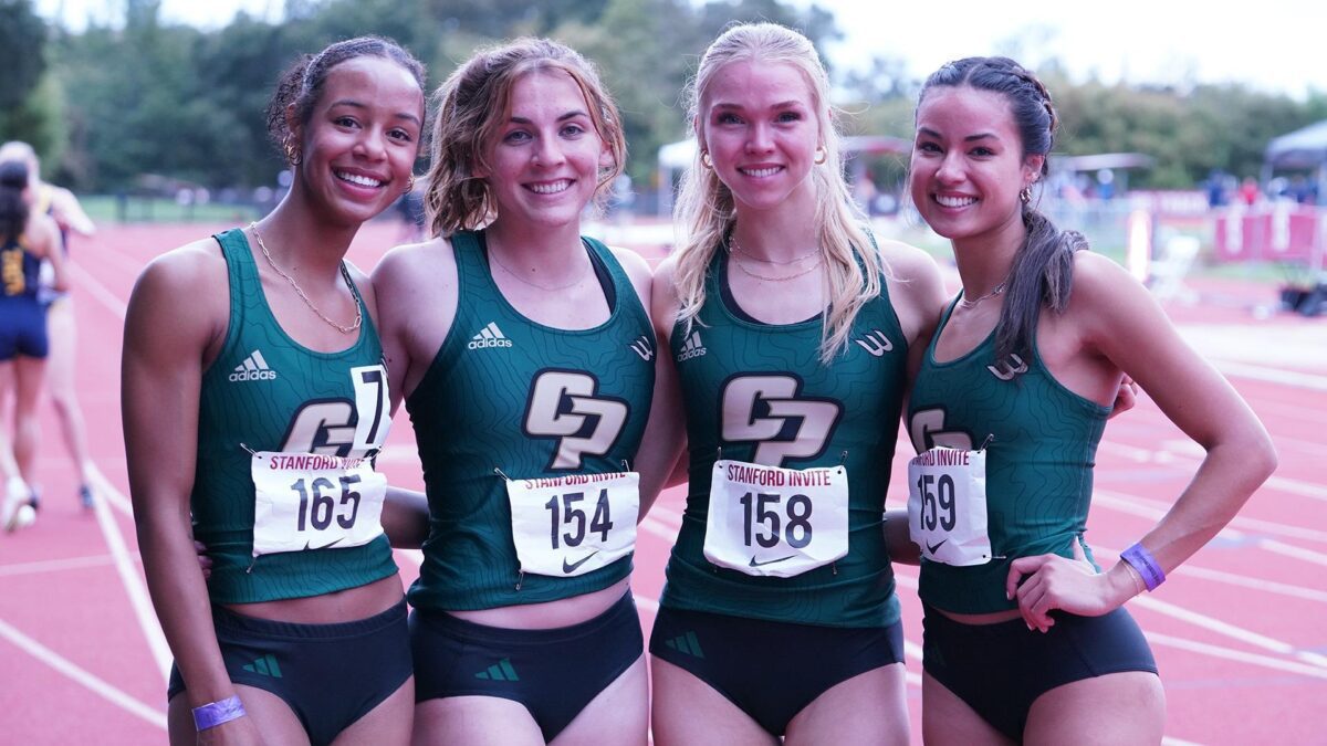 Four smiling female track athletes in green uniforms