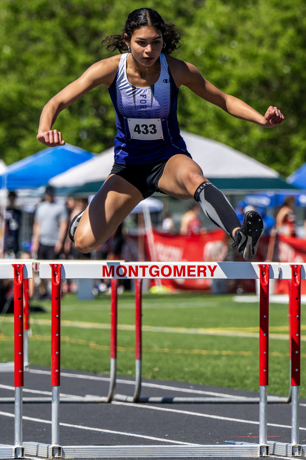 Female track athlete jumping over hurdle