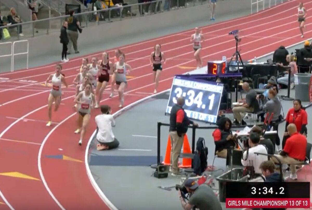 Athletes rounding indoor track beside large clock