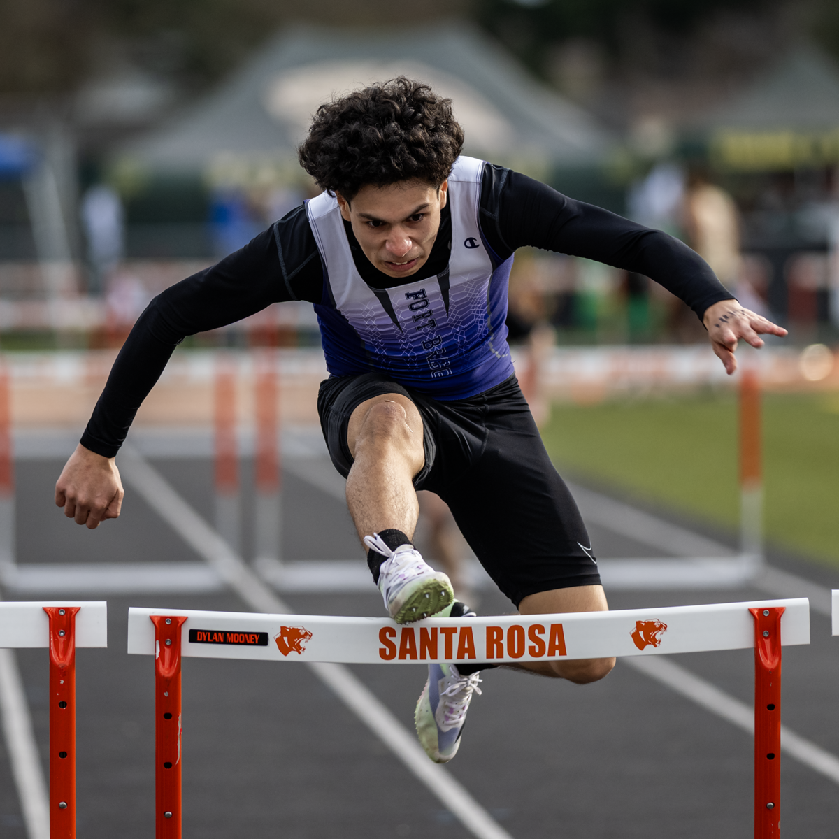 Curly-haired hurdler vaults over white barrier
