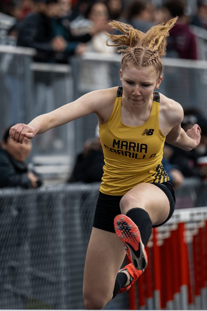 Female hurdler in yellow uniform clearing hurdle