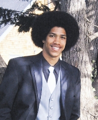 Young man in formal suit smiling outdoors by a tree.