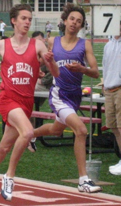 Two athletes sprinting during a track race, wearing red and purple uniforms.