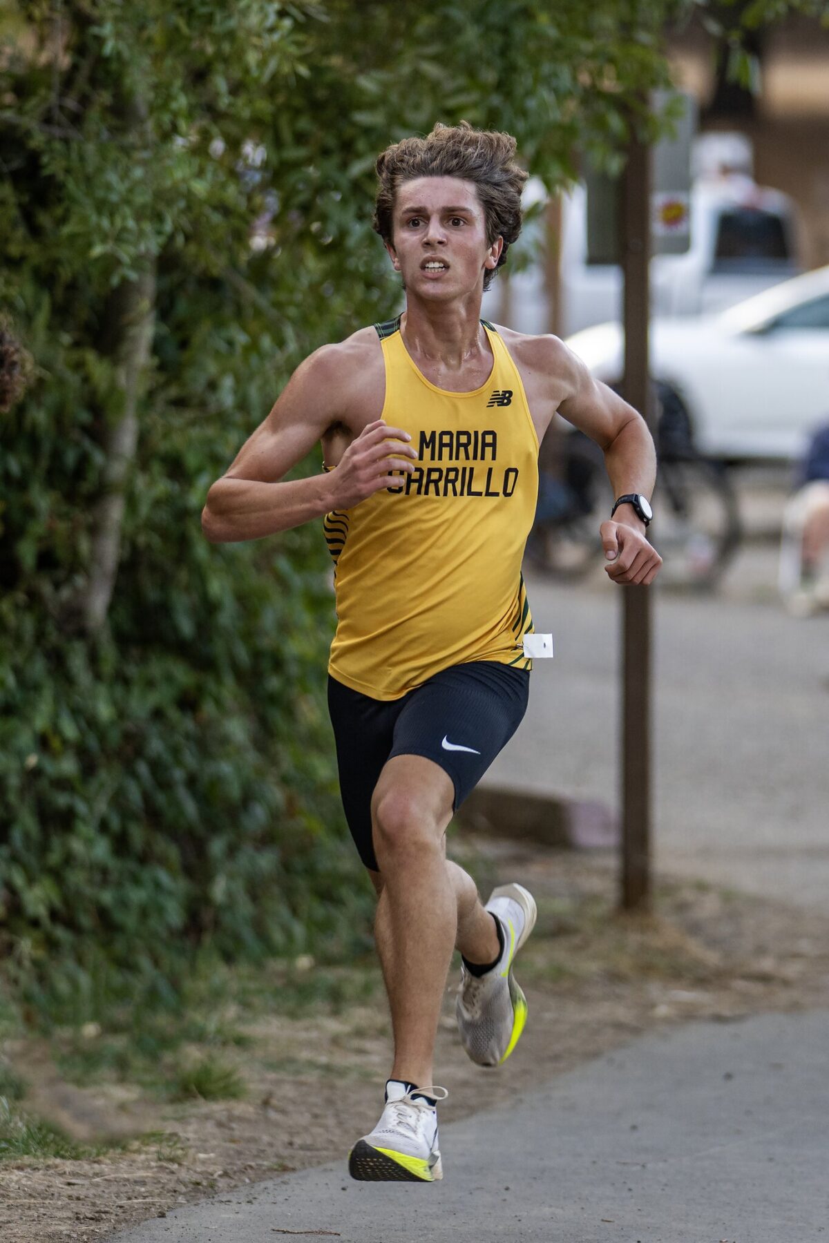 Runner in yellow shirt sprinting outdoors on a paved path.