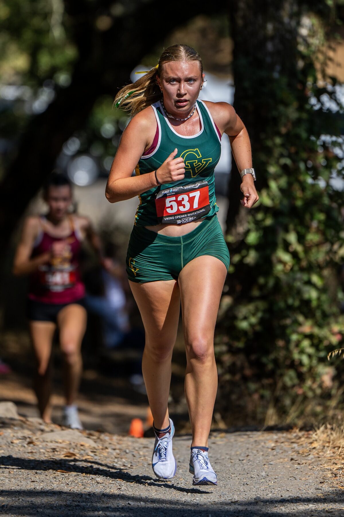 Female runner in green competing in a cross-country race, intensely focused.