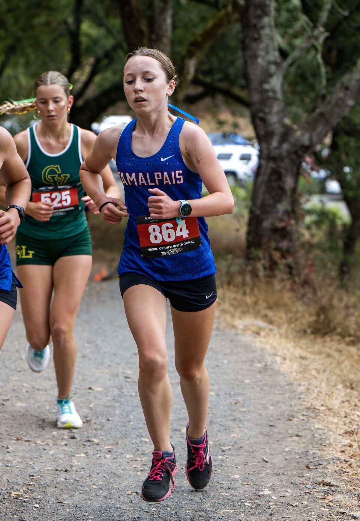 Female runners competing in a cross-country race on a wooded path.
