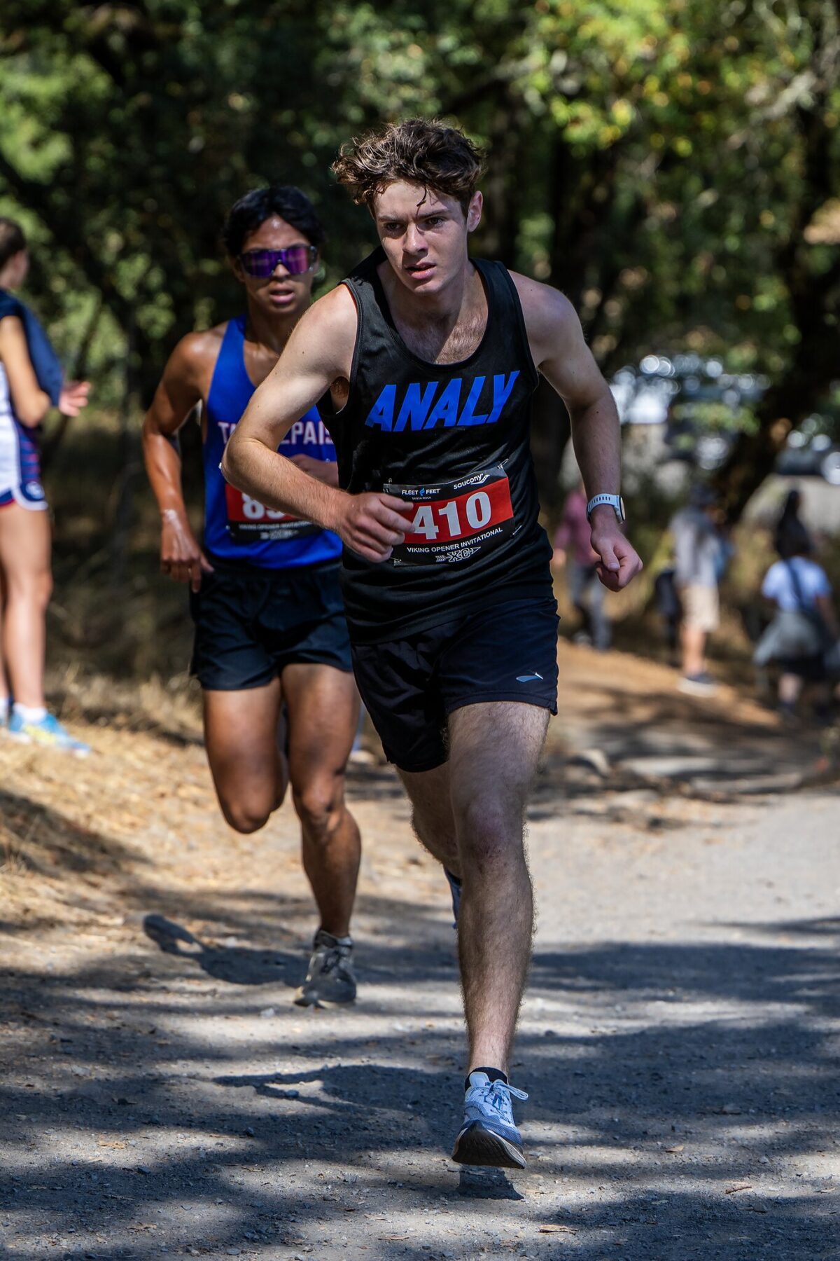 Male runner in a black outfit racing on a sunlit trail.