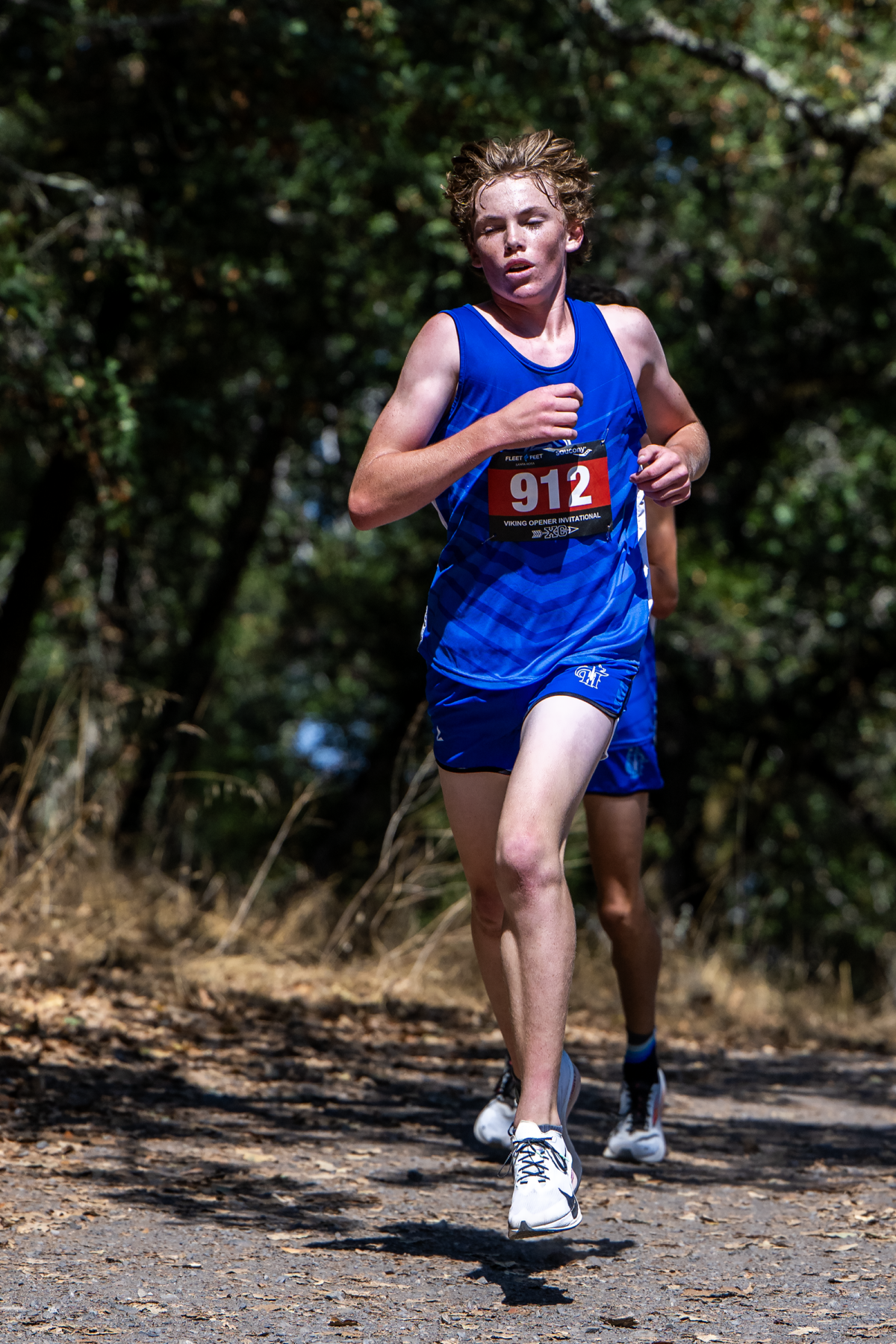 Young athlete running in a wooded trail race wearing a blue uniform and bib 912.
