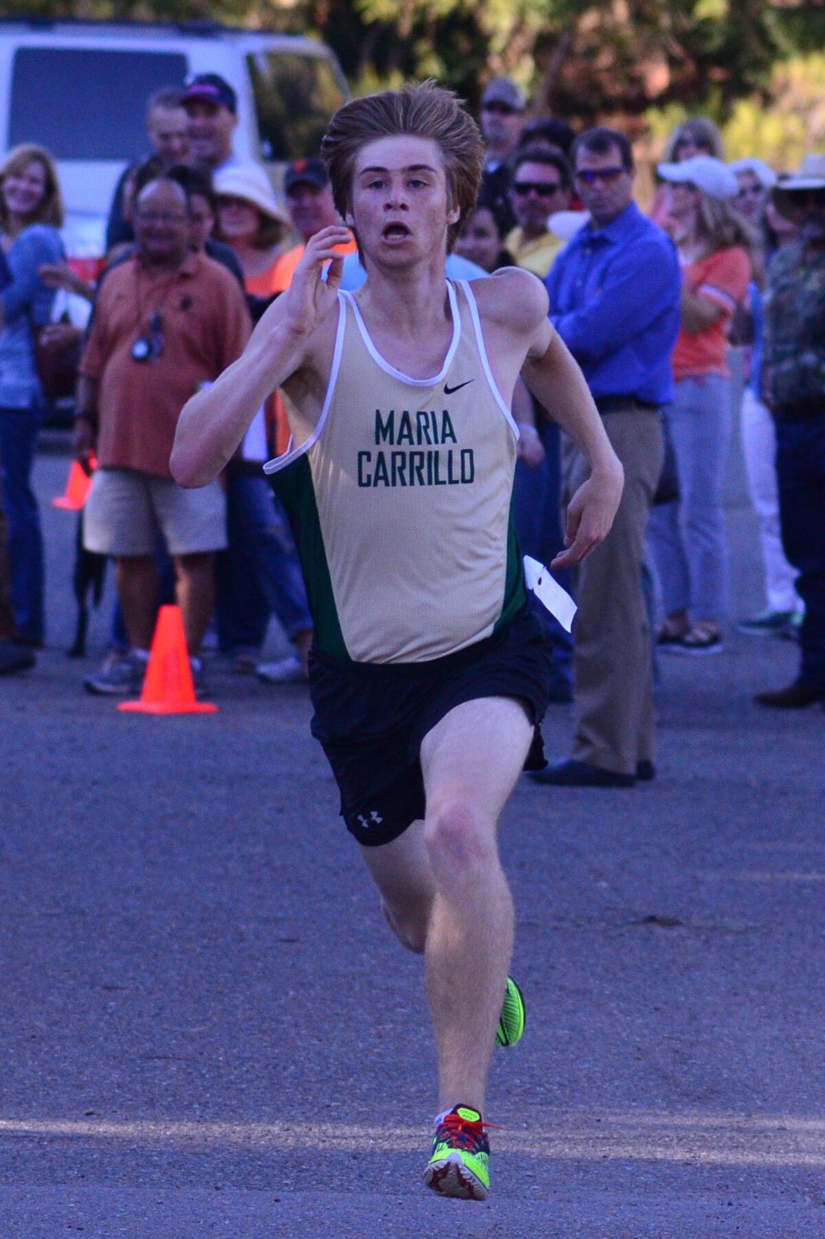 Young male runner in a white tank top competing in a race at dusk.