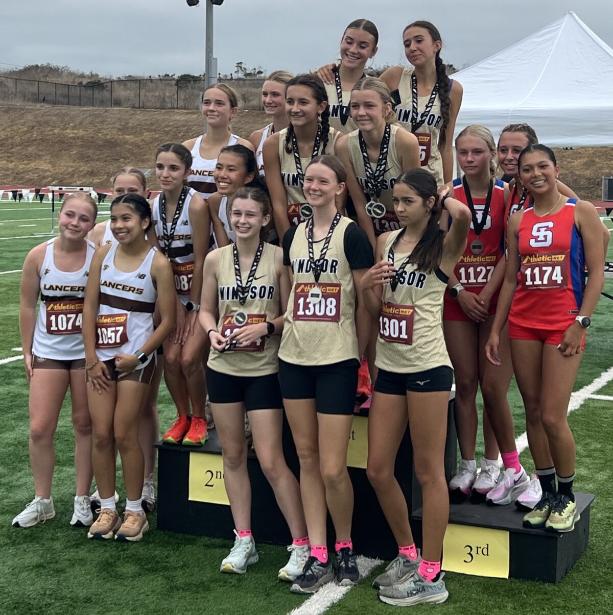 A group of female athletes posing after a race on a podium outdoors.