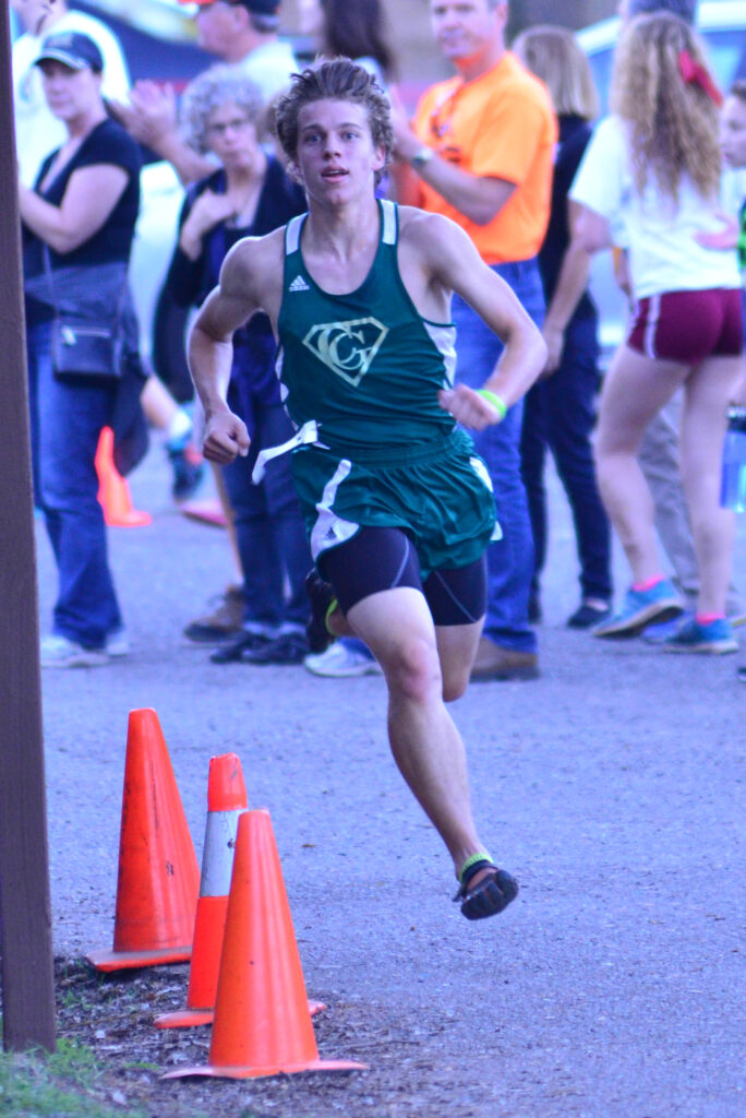 Runner in green uniform sprinting past orange cones during a race.