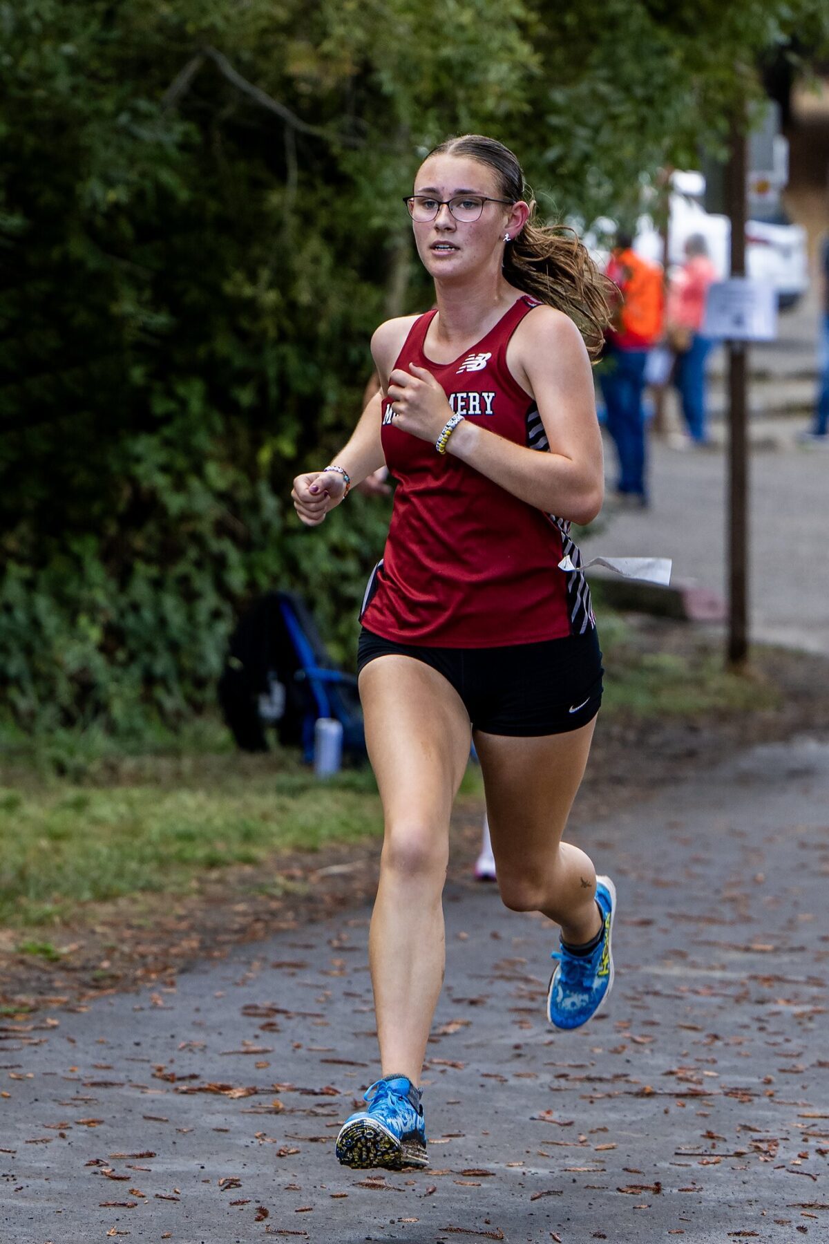 Female runner in maroon jersey and black shorts running outdoors on a paved path.