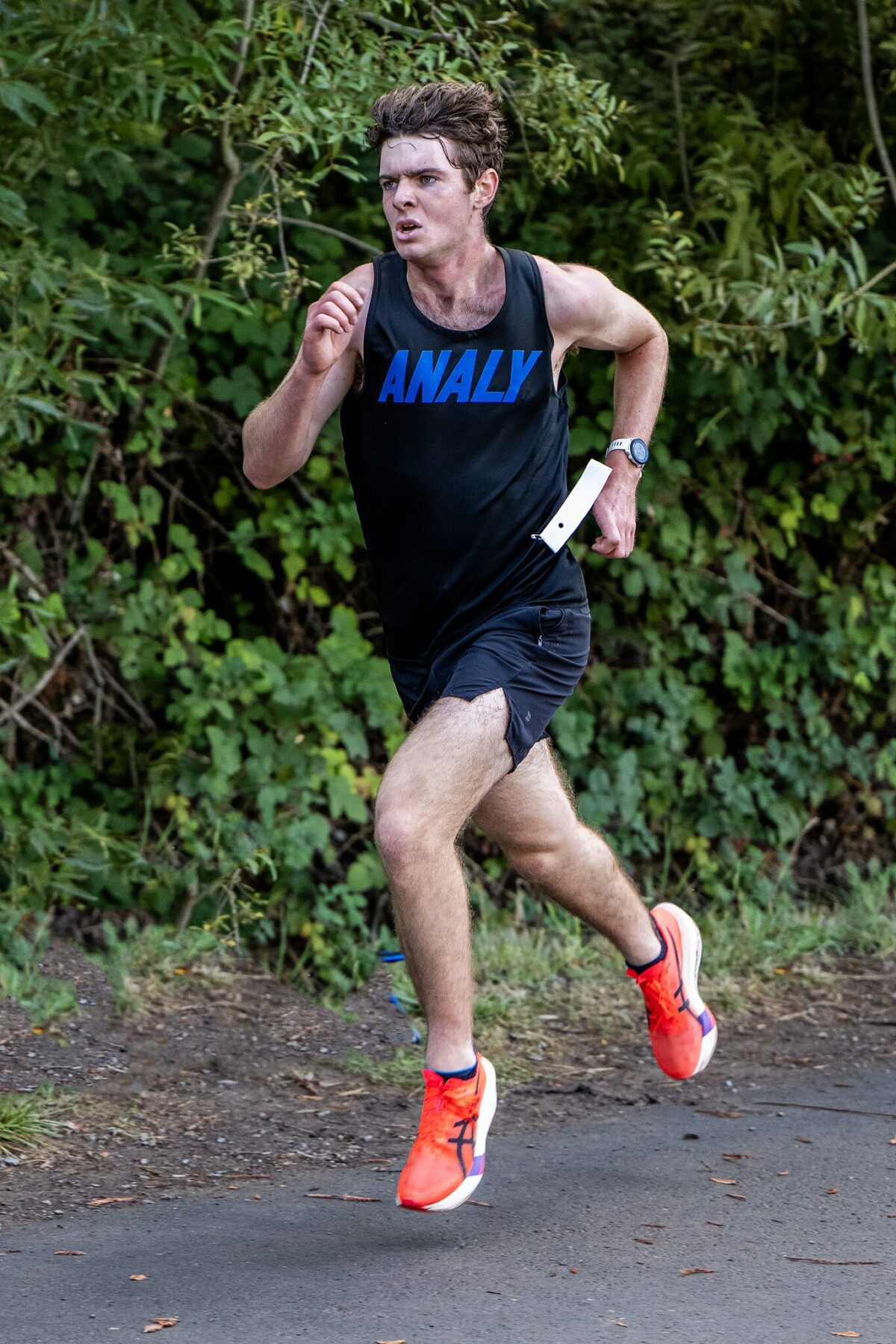 Runner in black tank top and red shoes jogging outdoors.