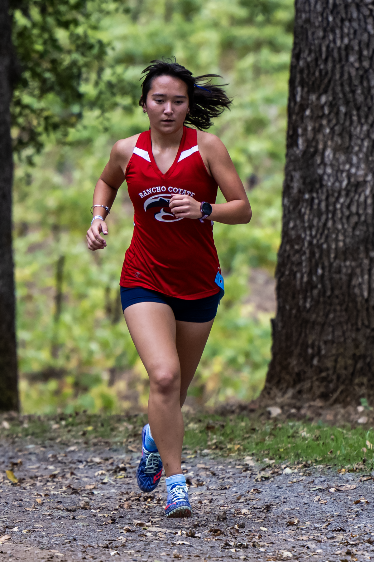 Young woman running on a forest trail in athletic gear.