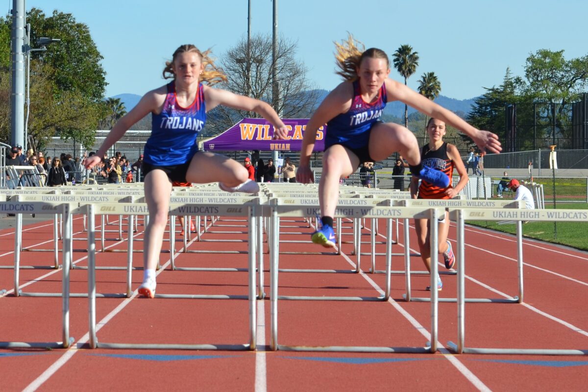 Two female athletes hurdling on outdoor track